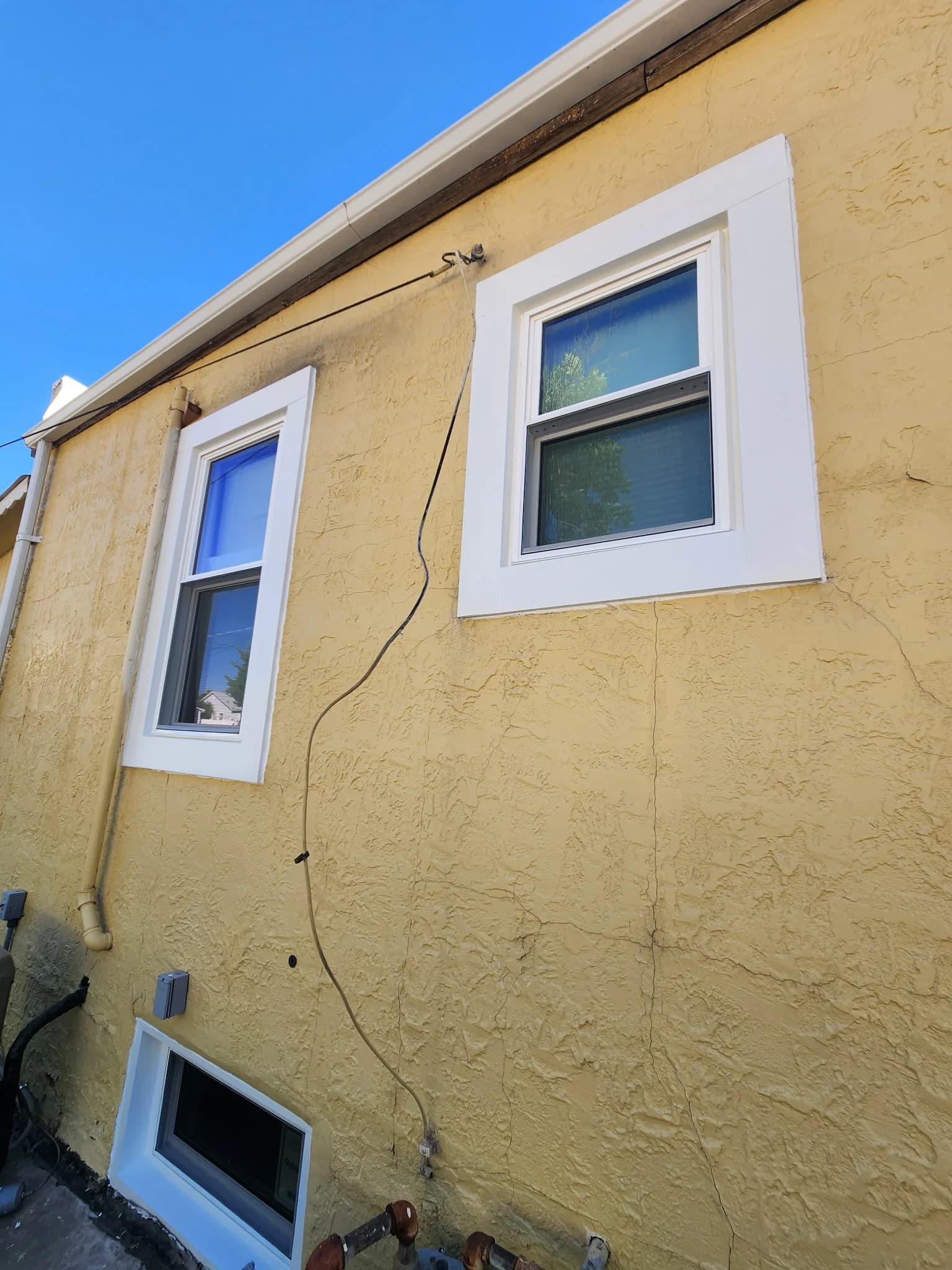 Small basement window in a stucco home exterior, set close to grade